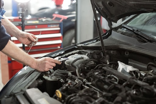 5 Reasons Why Your Garage Needs a Management System; a man working under the hood of an engine