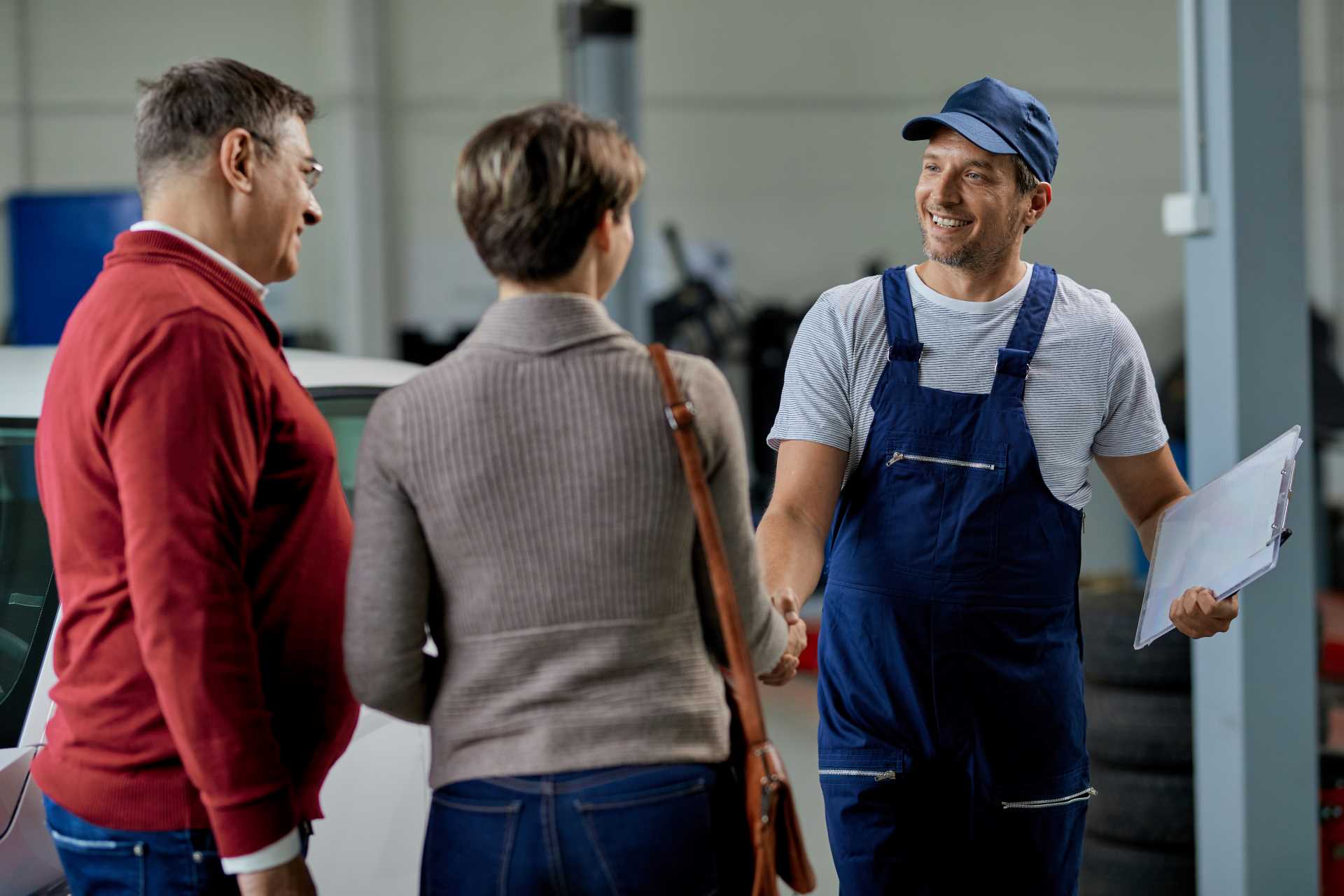 customer management, garage worker shaking hands with and smiling at a couple